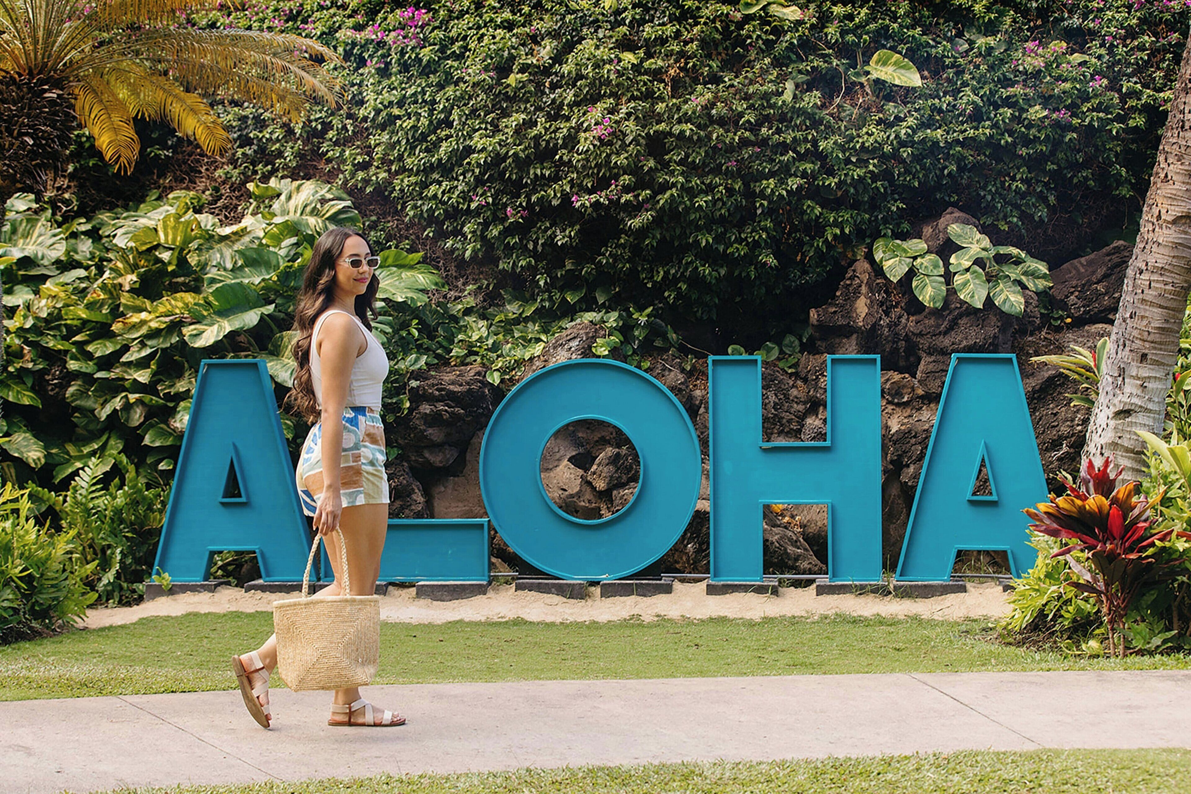 A woman walking in front of a large blue sign with the word "ALOHA".