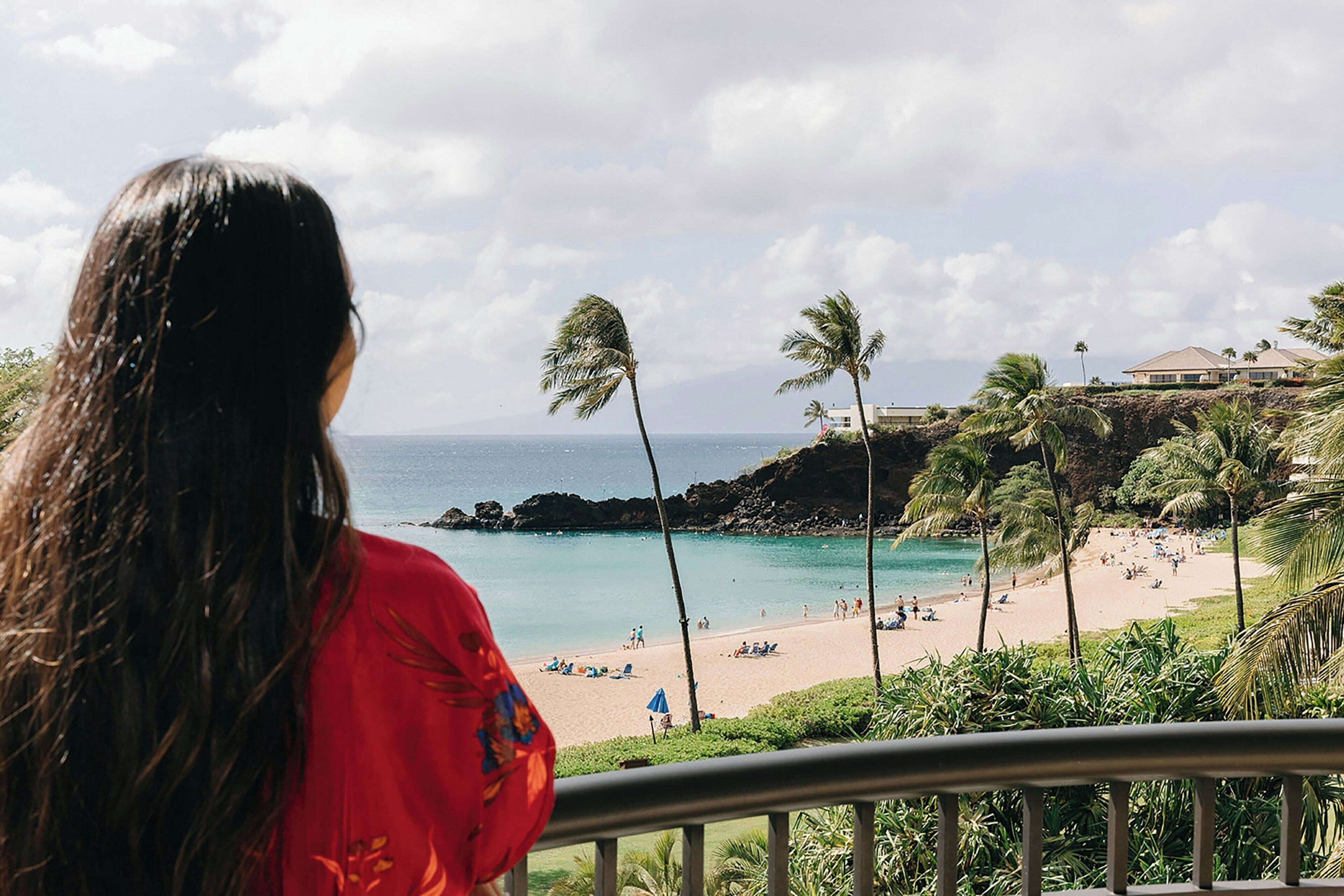 A balcony with a view of a beach, palm trees, and a distant building.