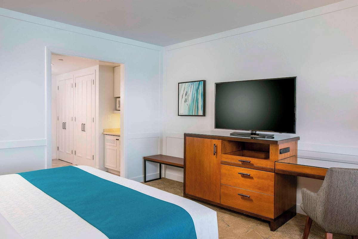 A hotel room with a bed, a wooden desk with a television, a bench, and a wardrobe.