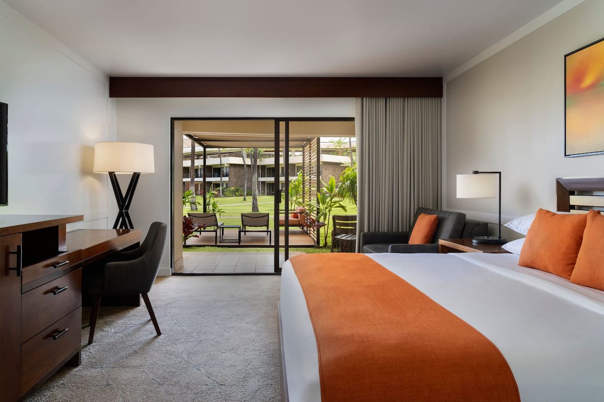 A hotel room with a large bed, a desk, a chair, and a view of the outdoor area.