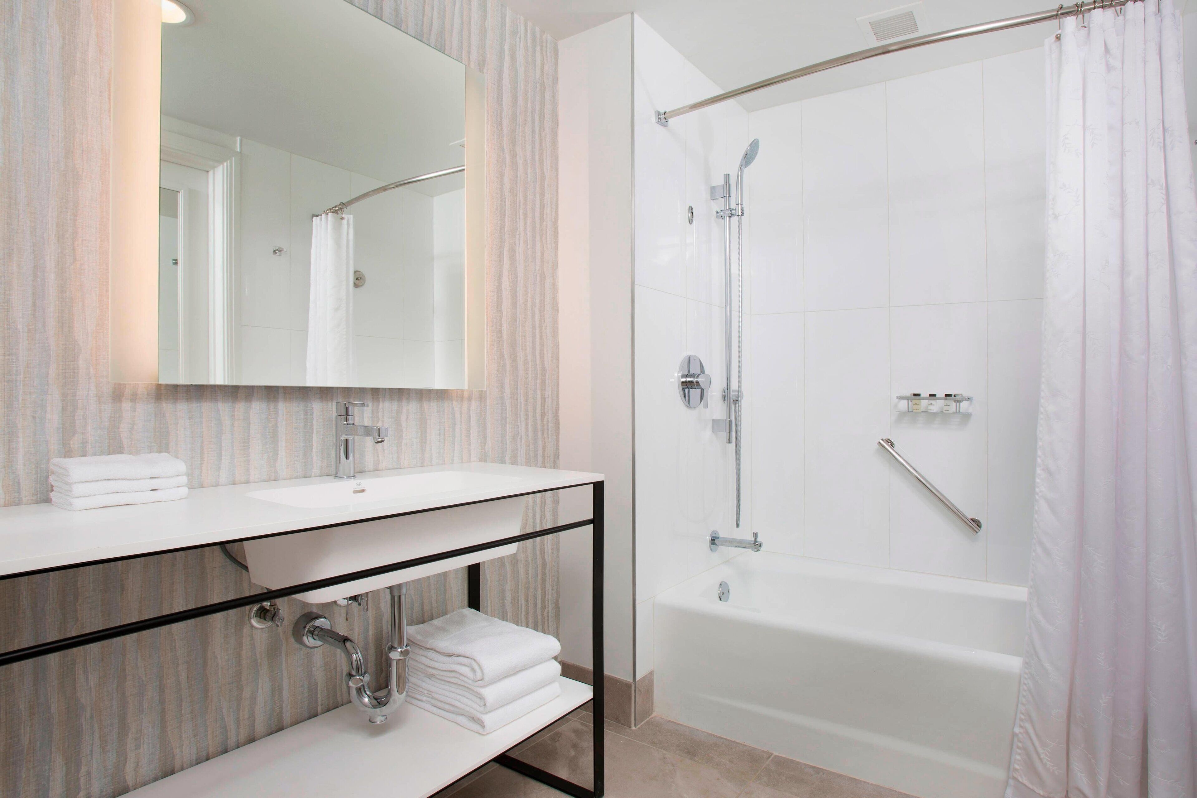 A modern bathroom with a glass shower enclosure, a white bathtub, and a vanity with a mirror and towel rack.