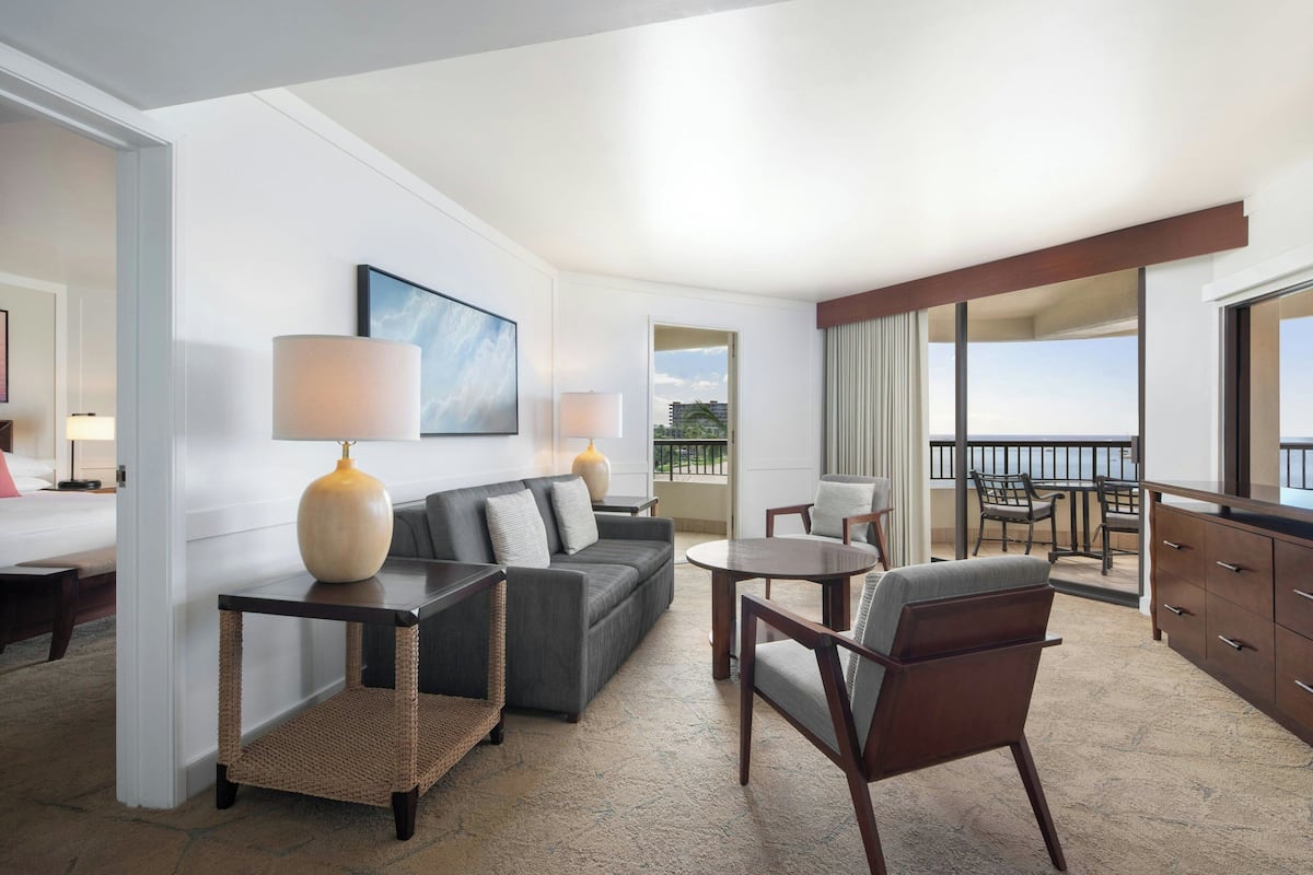 A modern hotel room with a sofa, armchairs, a small table, and a balcony with a view.