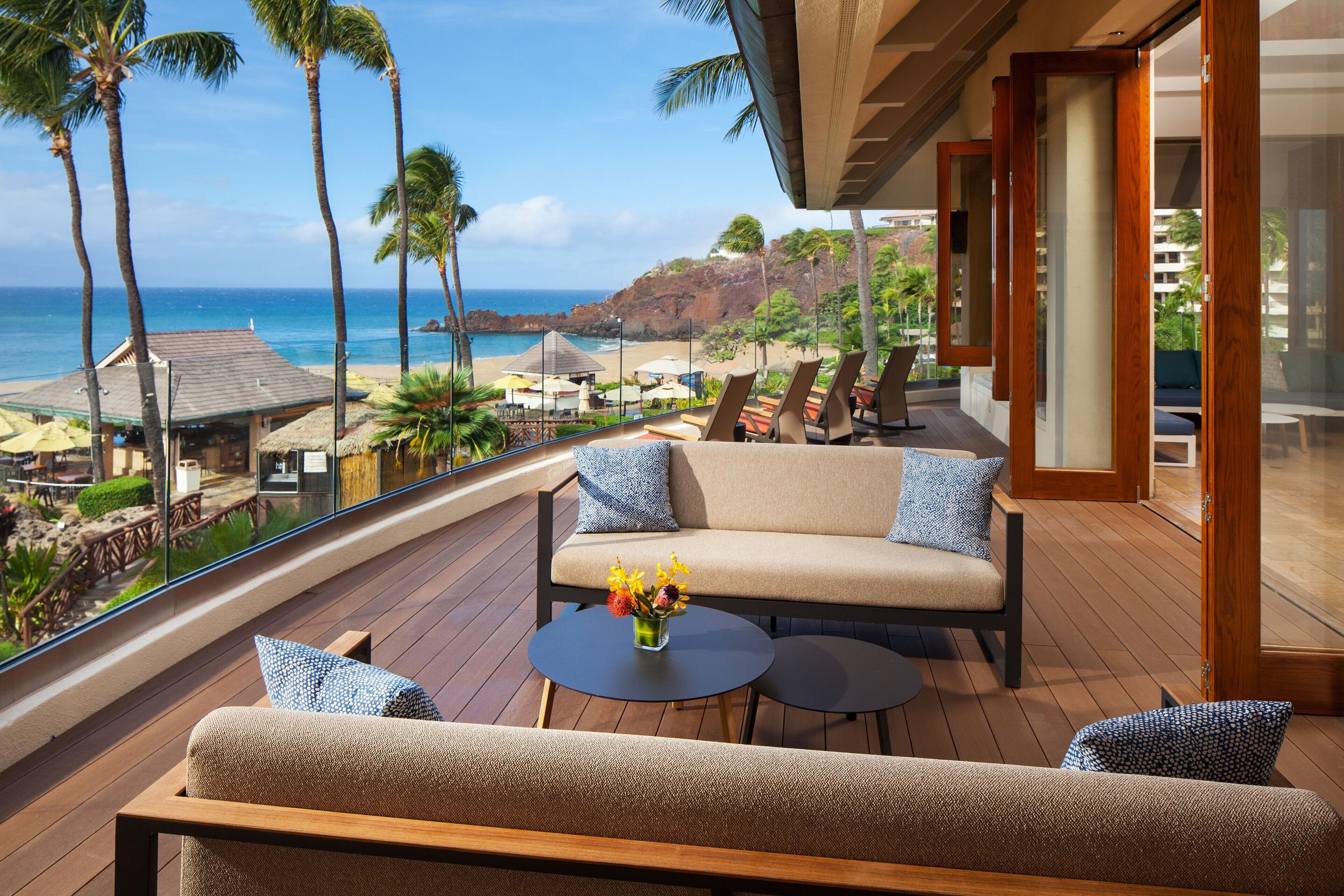 Un balcon avec un canapé et des fauteuils, donnant sur une plage et l’océan.