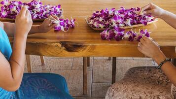 Una mesa de madera con flores moradas y blancas, y una persona ensartándolas con un hilo.