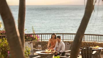 Una pareja cenando en una mesa al aire libre con un brasero, con vista al mar.