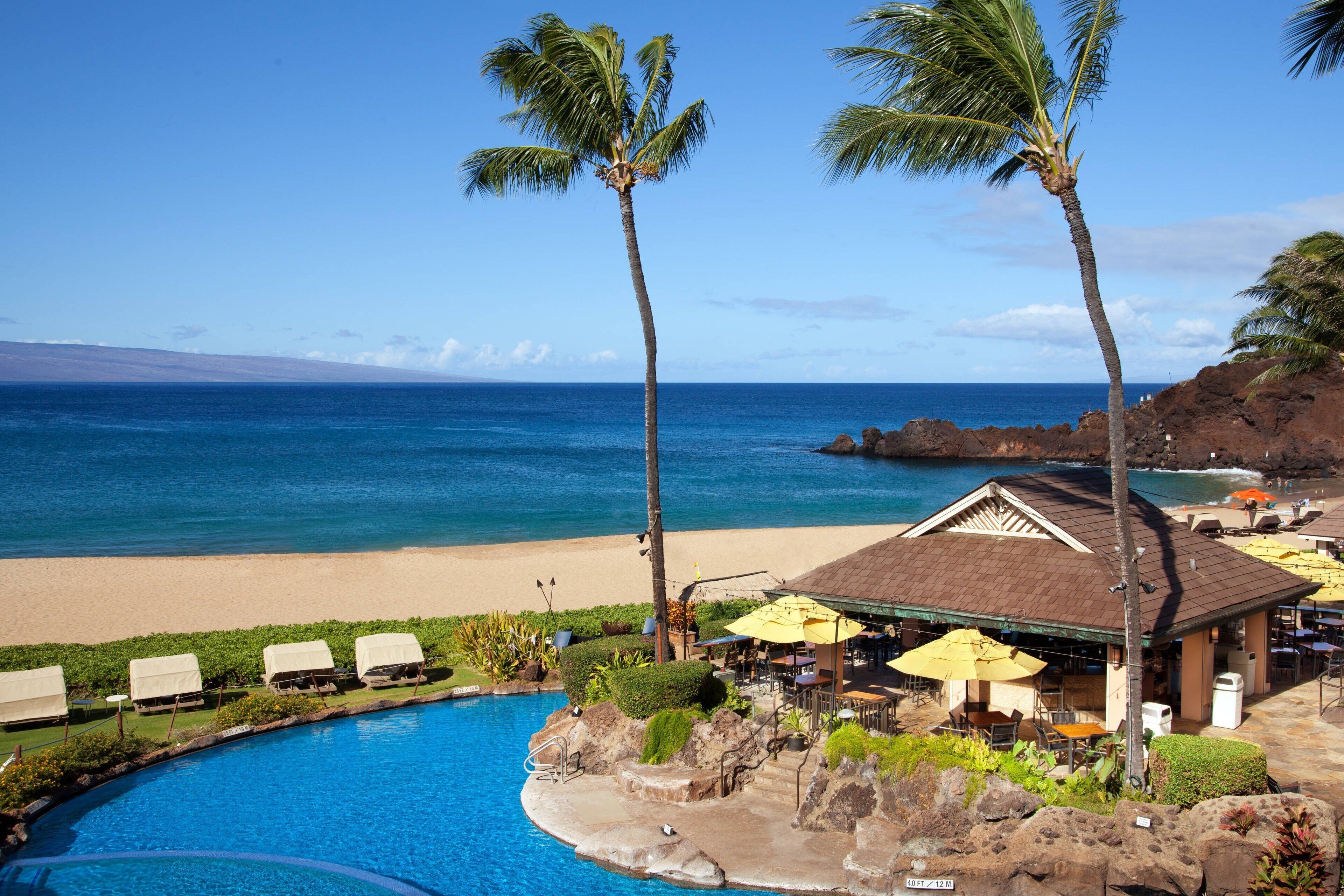 A poolside area with lounge chairs, a covered seating area, and a view of the ocean.