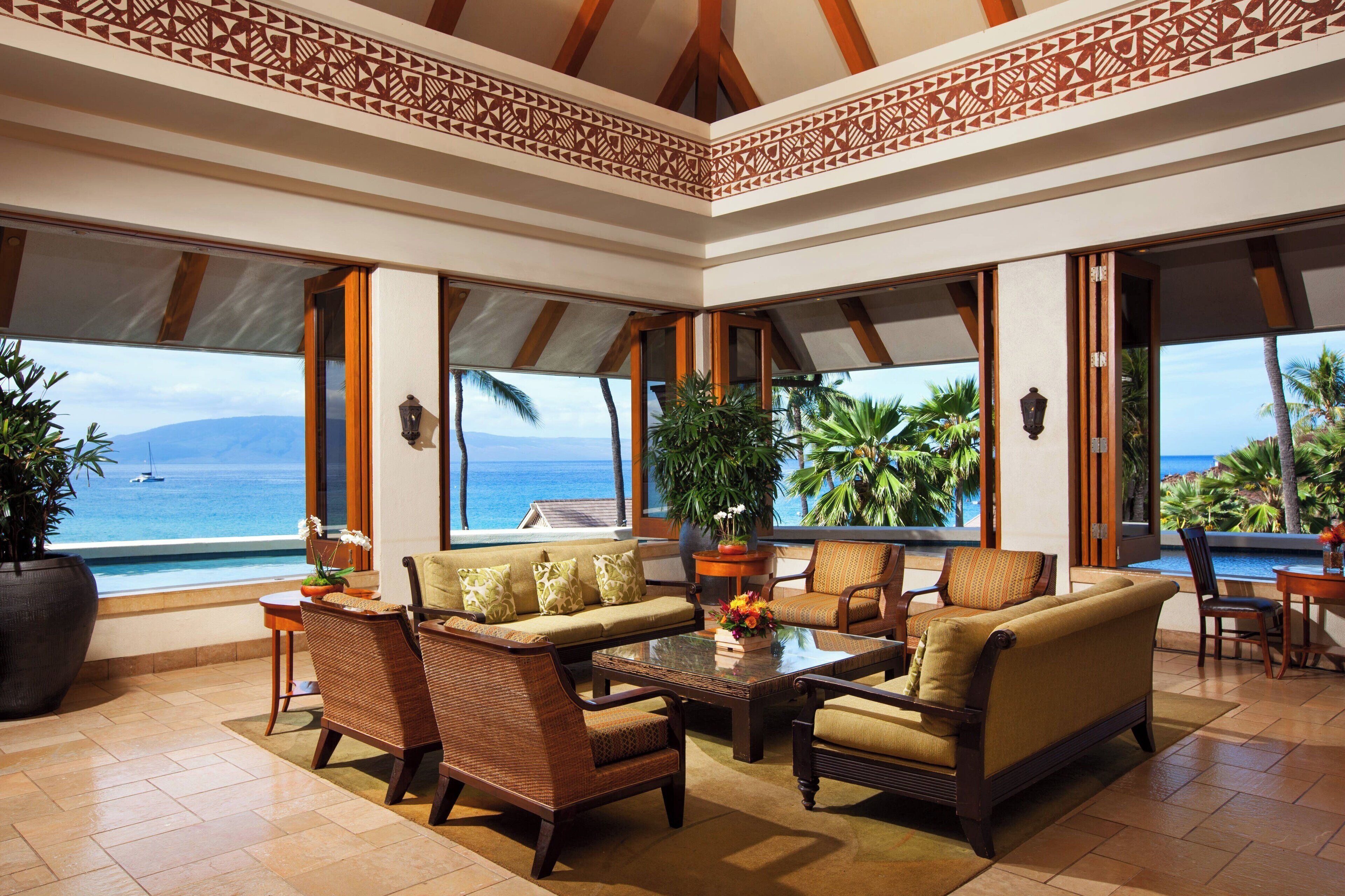 A spacious lounge with a large window offering a view of the ocean and palm trees.