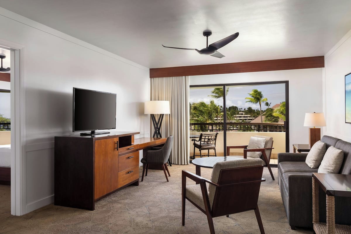 A hotel room with a flat-screen TV, wooden desk, and comfortable seating area with a balcony view.