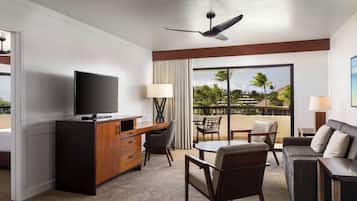 Een hotelkamer met een flatscreen televisie, een houten bureau en een zithoek met balkon.
