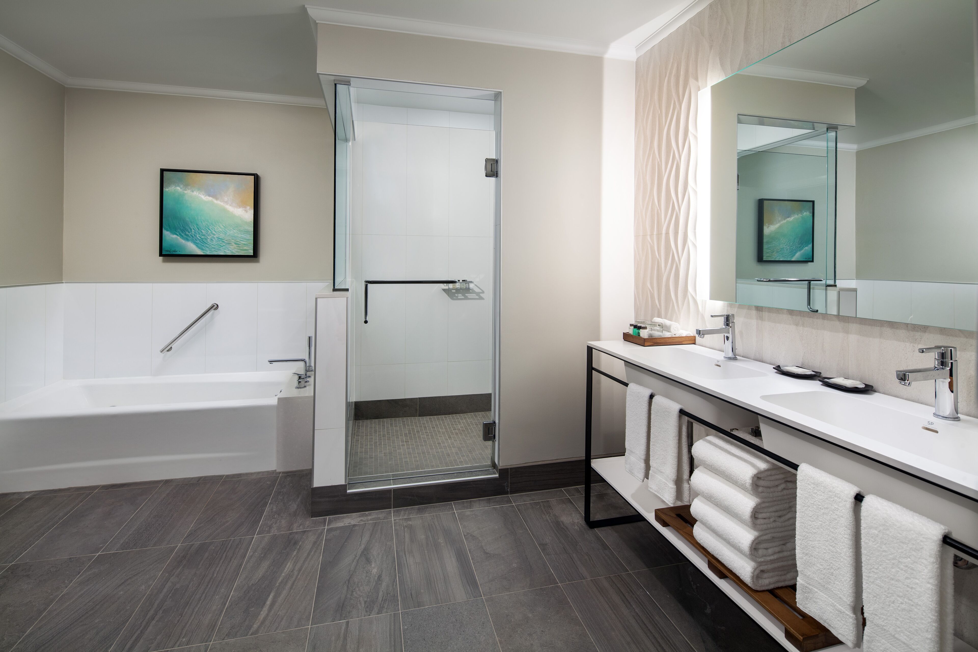 Un baño moderno con bañera, cabina de ducha de vidrio, tocador con espejo y un perchero para toallas.