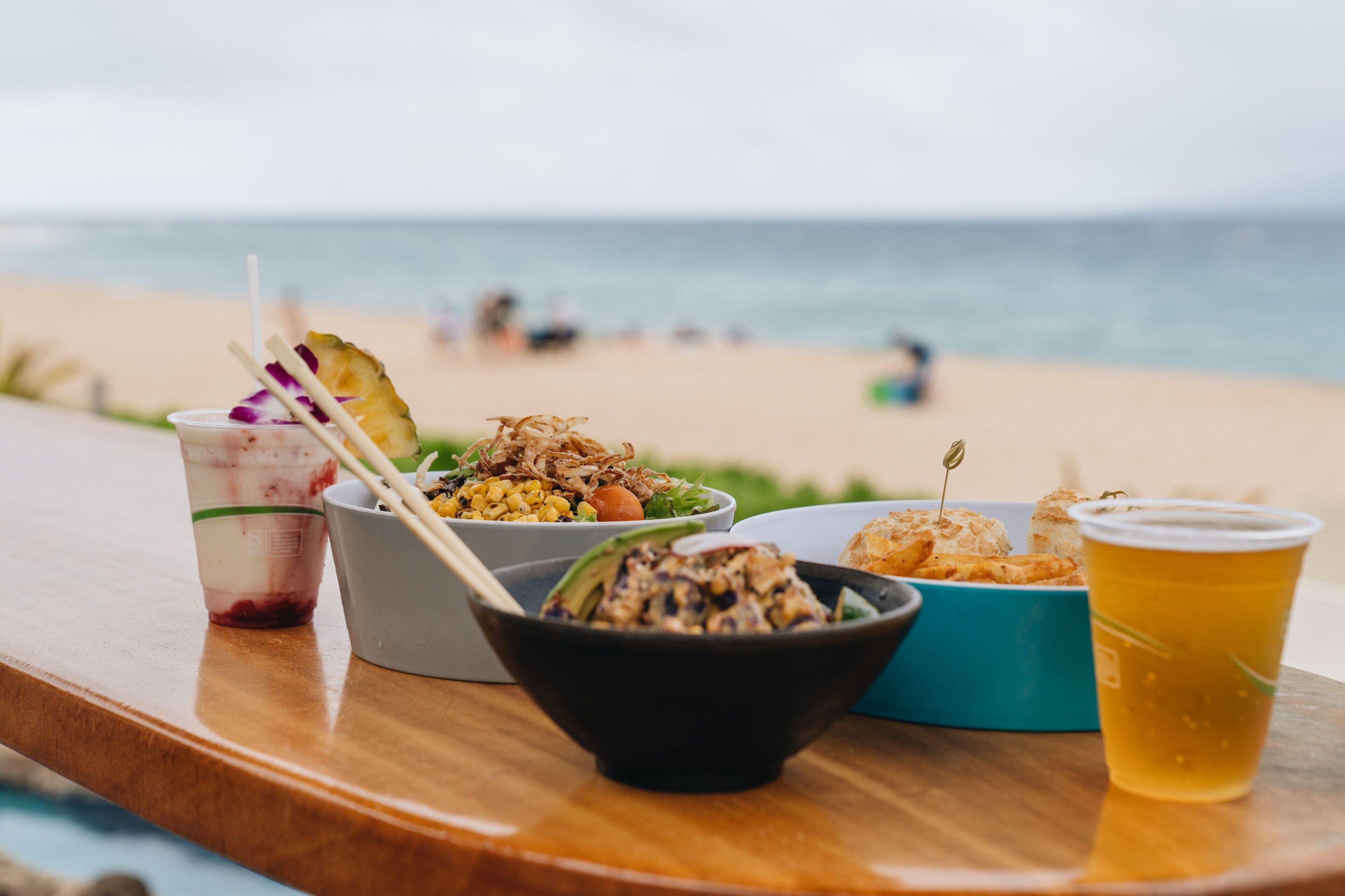 A table with various dishes and drinks on a beach setting.