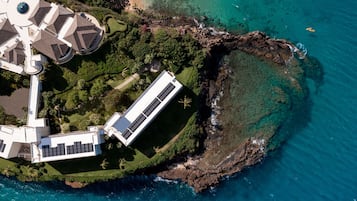 An aerial view of a coastal property with a modern building, a swimming pool, and a rocky shoreline.