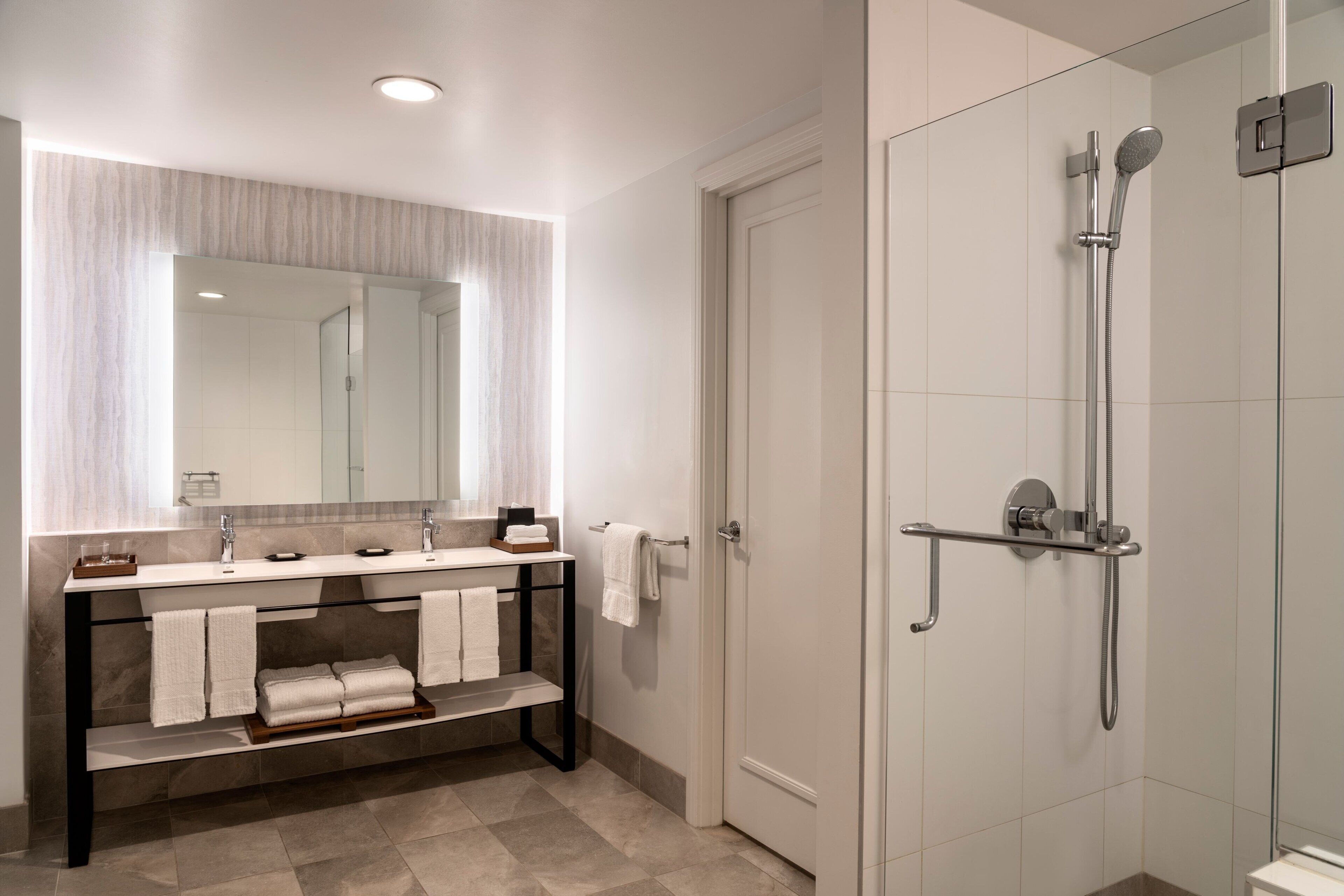 Un baño moderno con cabina de ducha de vidrio, tocador con espejo y perchero para toallas.