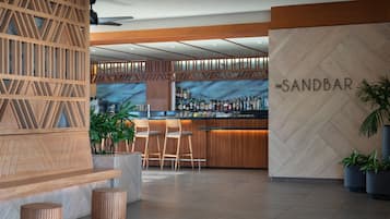A modern bar area with a wooden partition, bar stools, and a wall with the name 'The Sandbar'.