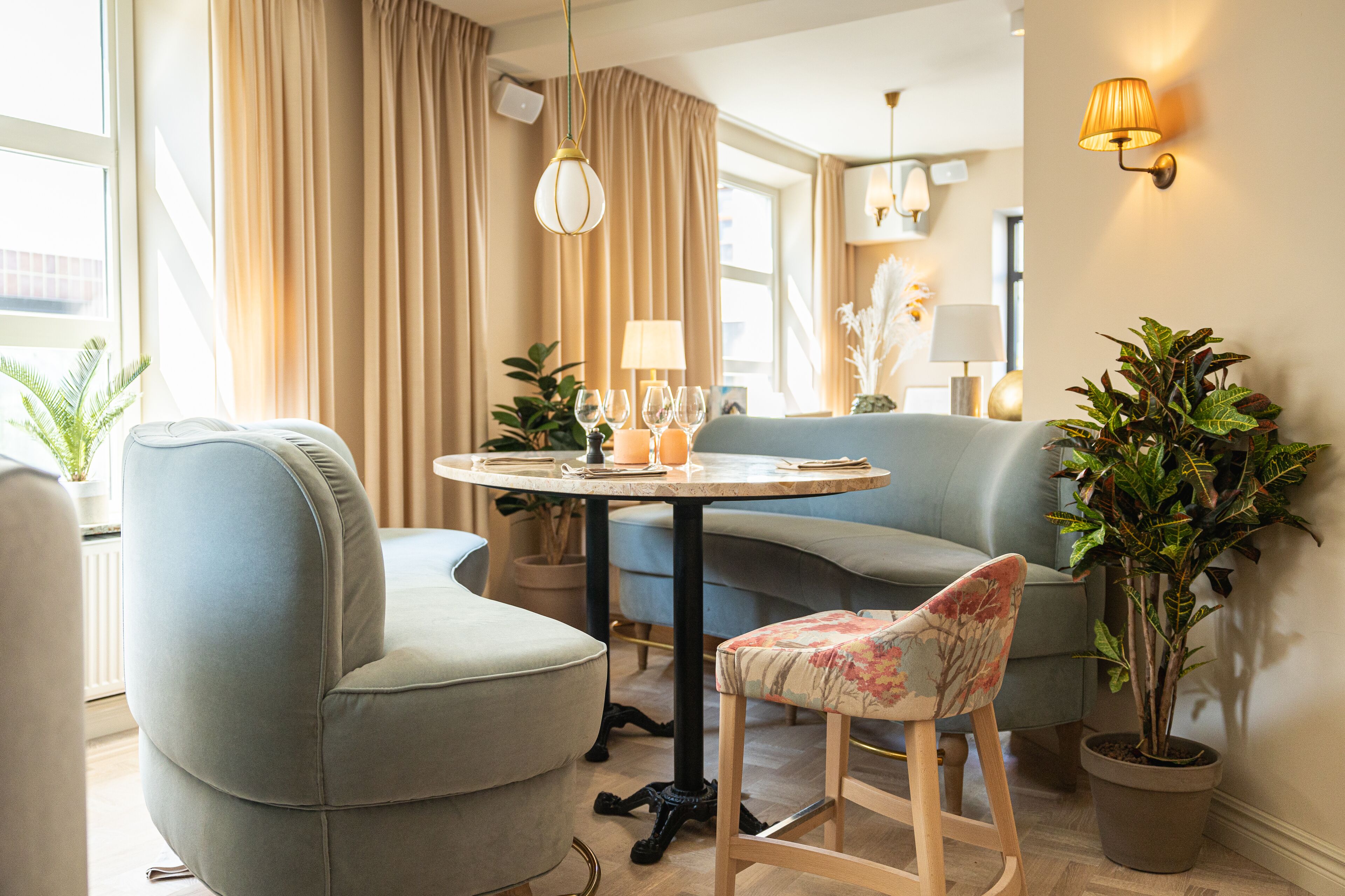 Una sala de estar moderna con una mesa redonda, un sofá y una silla. Hay plantas en macetas y lámparas de pared.