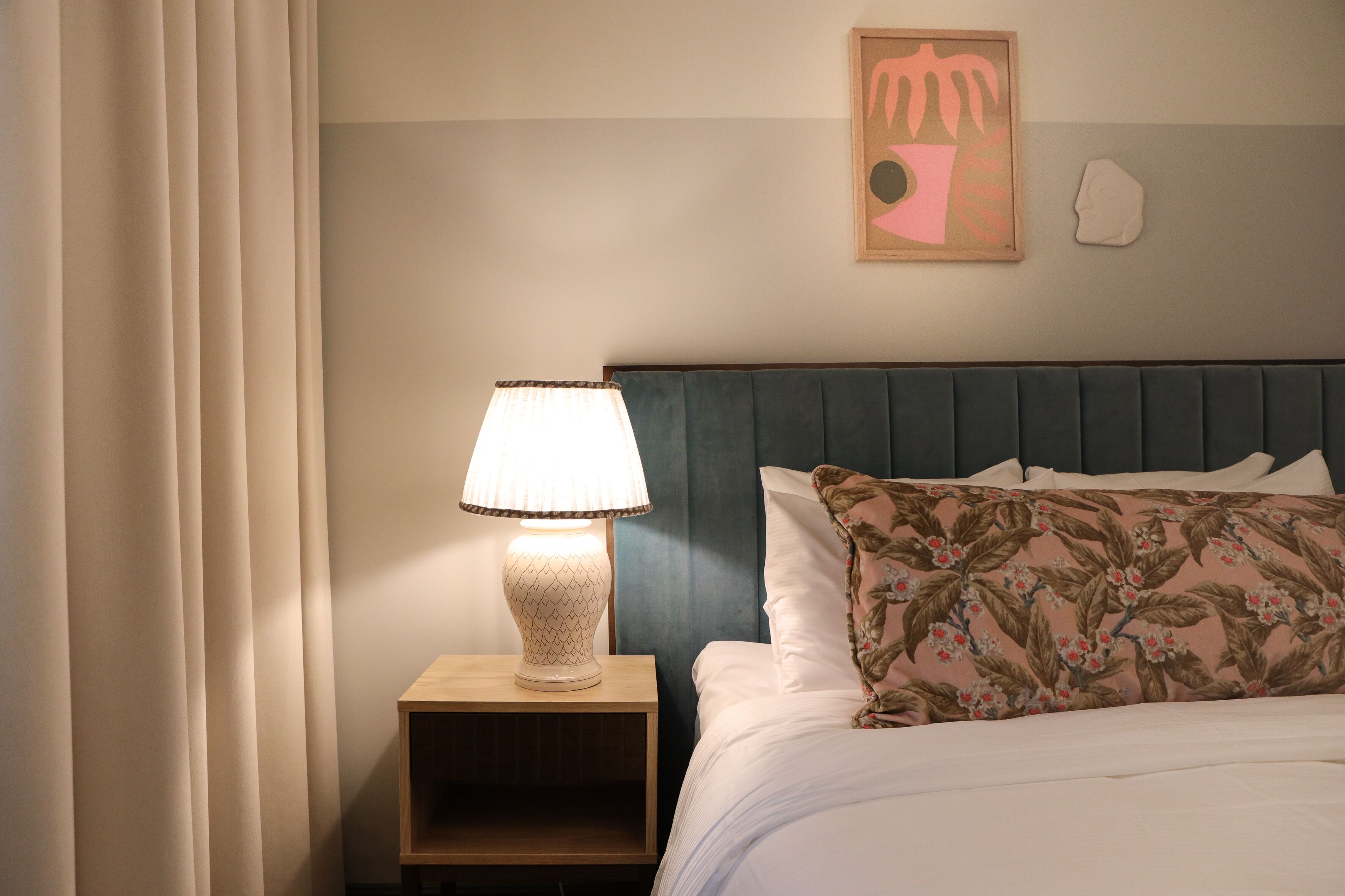 A neatly made bed with a floral pillow, a bedside lamp, and a framed artwork on the wall.