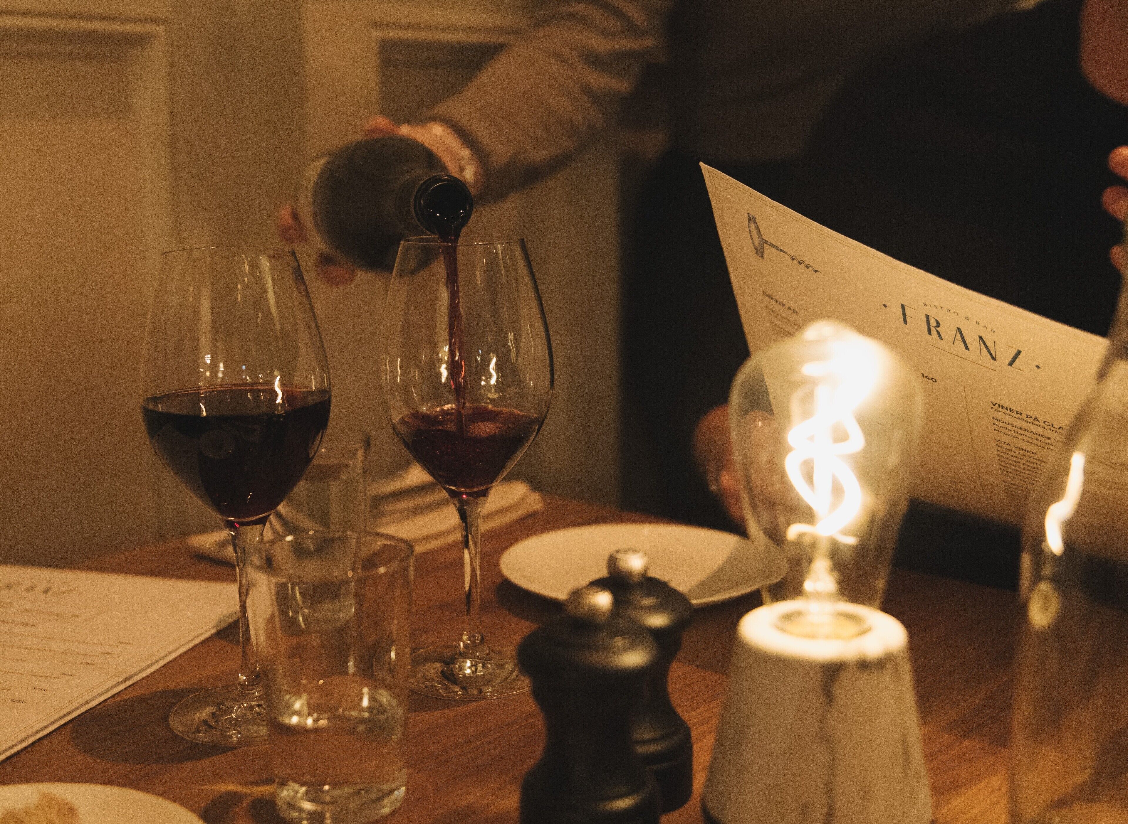 Una mesa con copas de vino, una carta y un salero.