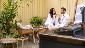 A couple in white robes sitting on wicker chairs in a spa-like setting with a massage table and a small table with a candle. - Elite Hotel Mårtenson (Halmstad)