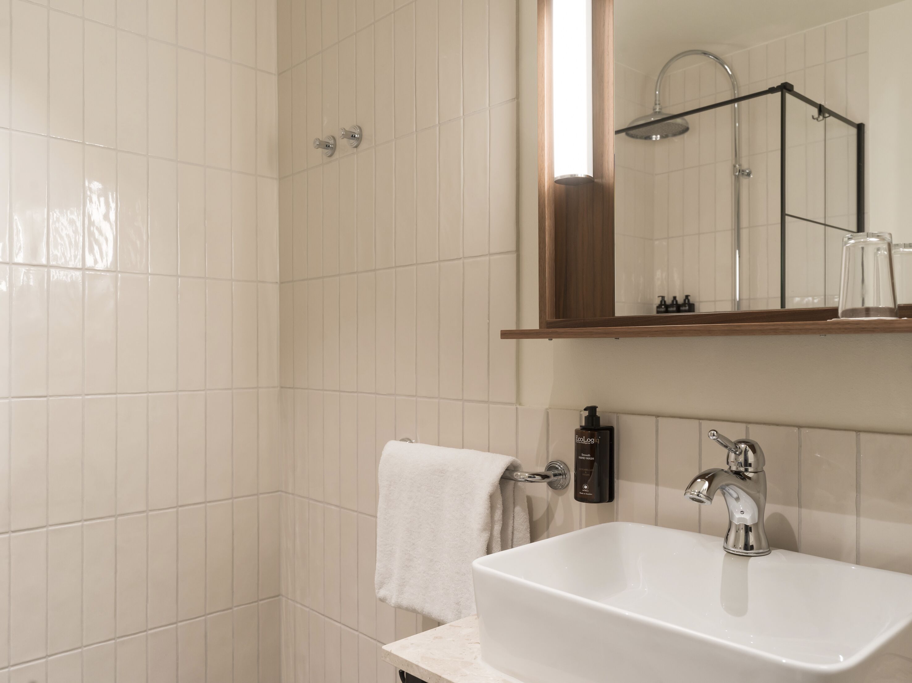 Un baño con azulejos blancos, un lavamanos blanco, un espejo y una ducha.