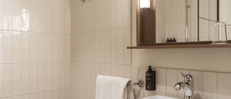 Un baño con azulejos blancos, un lavamanos blanco, un espejo y una ducha.