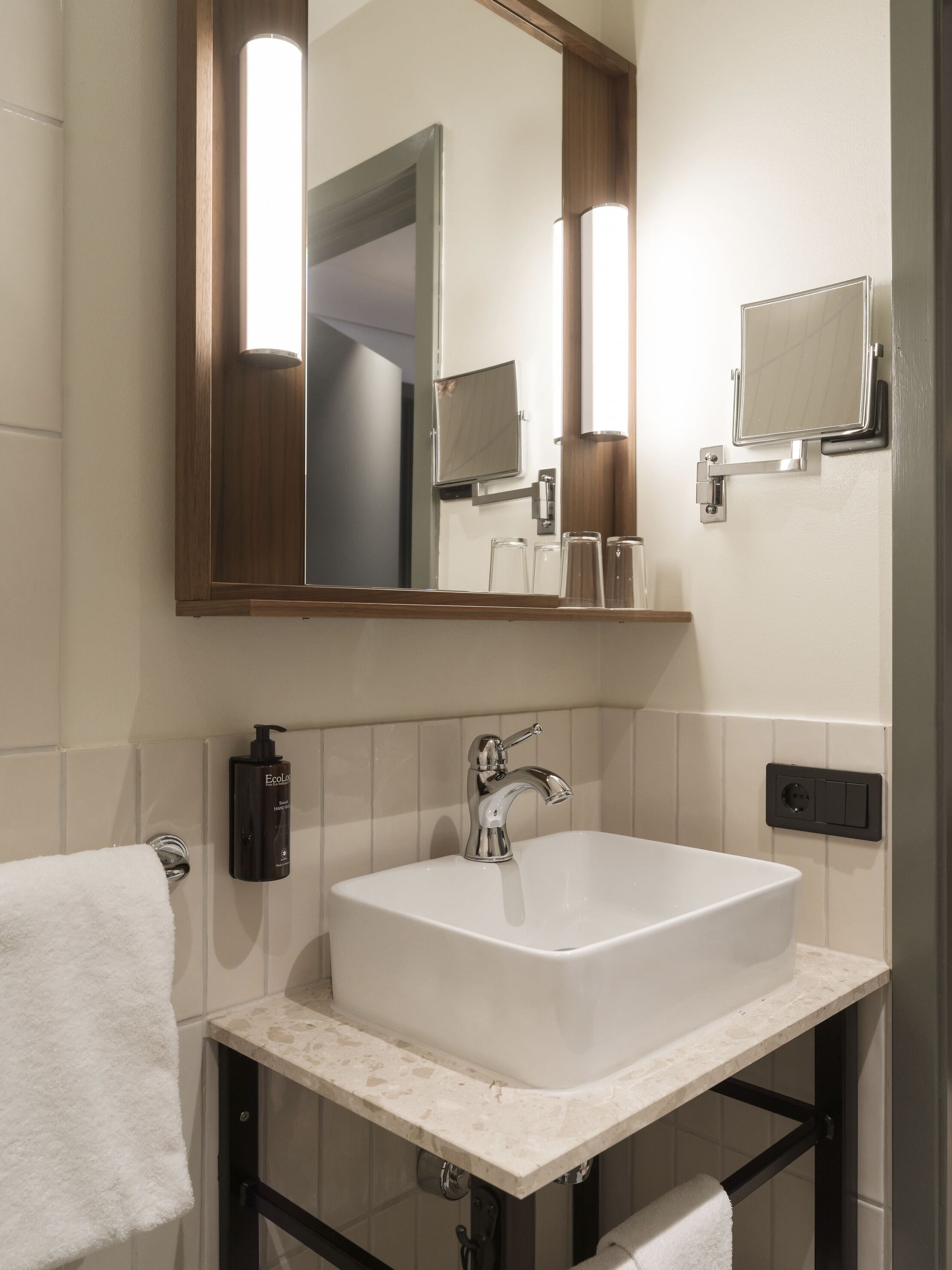 Un baño con un lavamanos blanco, un espejo y un perchero para toallas.