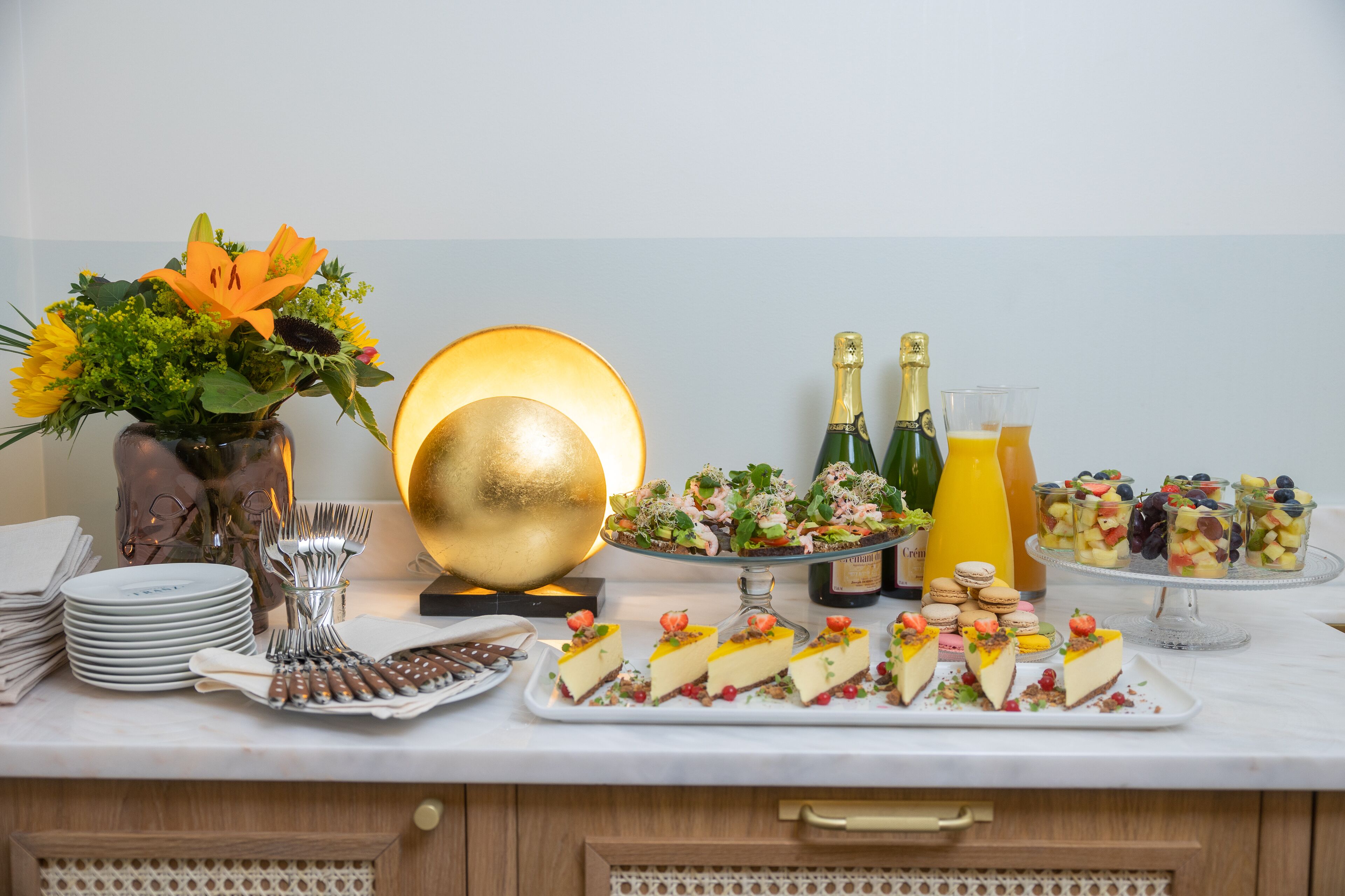 En buffet med forskellige retter, herunder desserter og frugt, samt en vase med blomster.