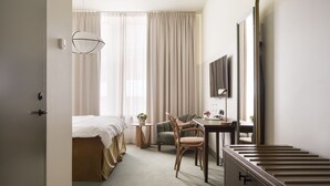 A hotel room with a bed, a desk, a chair, a small table with a plant, and a large mirror. - Elite Hotel Mårtenson (Halmstad)