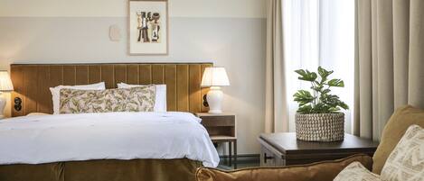 Habitación de hotel con una cama grande, dos lámparas de noche, una mesita de noche con una planta y una ventana con cortinas.
