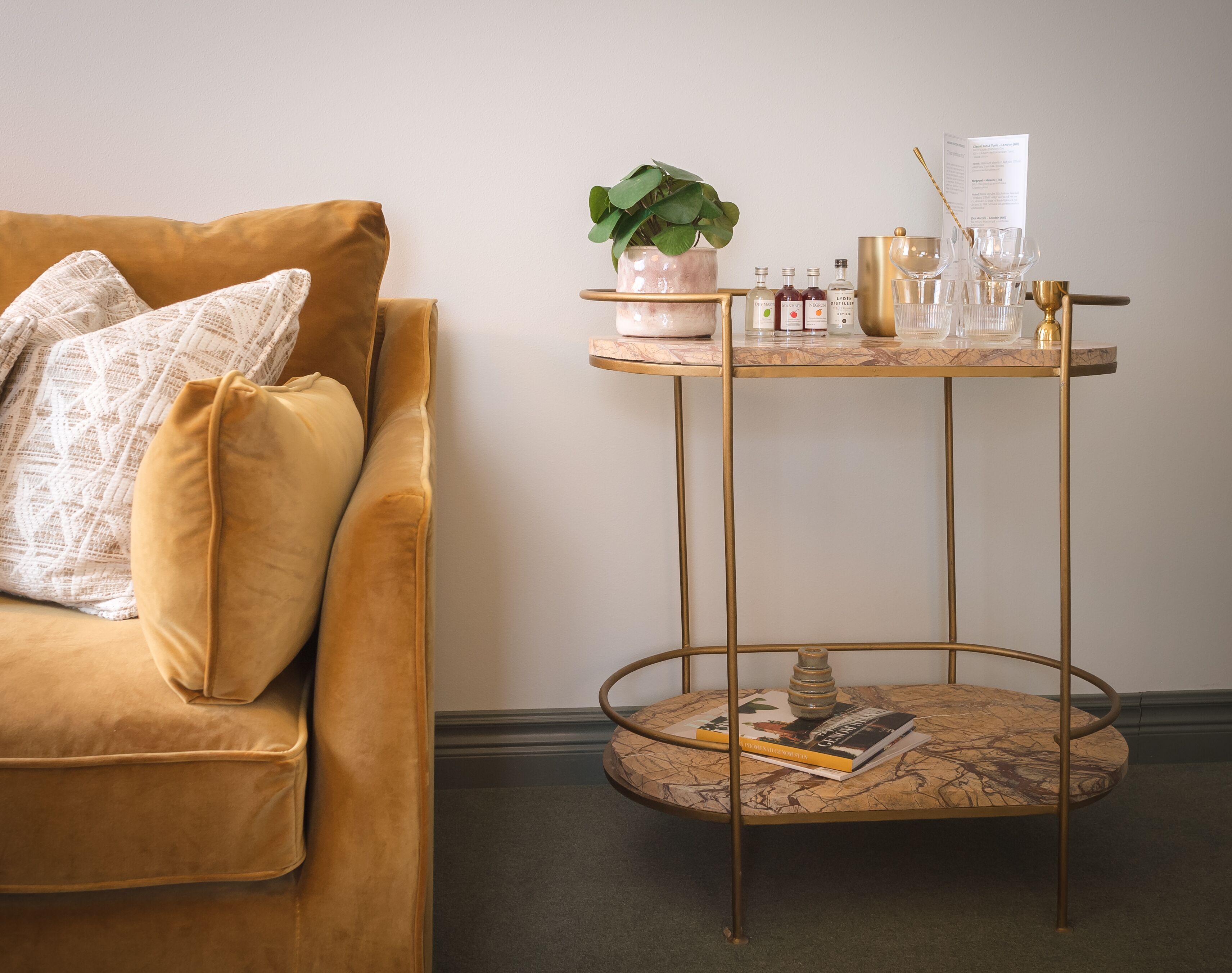 Un salon chaleureux avec un canapé de couleur moutarde, une petite table basse ronde au plateau en marbre et une table d’appoint haute avec des finitions dorées.