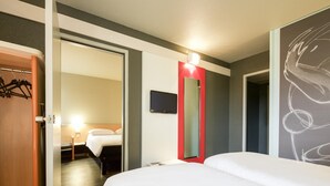 A hotel room with a bed, a TV, a mirror, and a door leading to another room. - ibis Pau Lescar (Lescar)