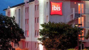 A hotel with a prominent 'ibis' sign, multiple windows, and a staircase on the right side. - ibis Pau Lescar (Lescar)