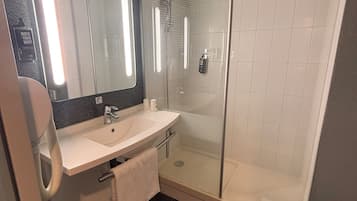Un baño moderno con cabina de ducha de vidrio, un lavabo blanco y un espejo grande.
