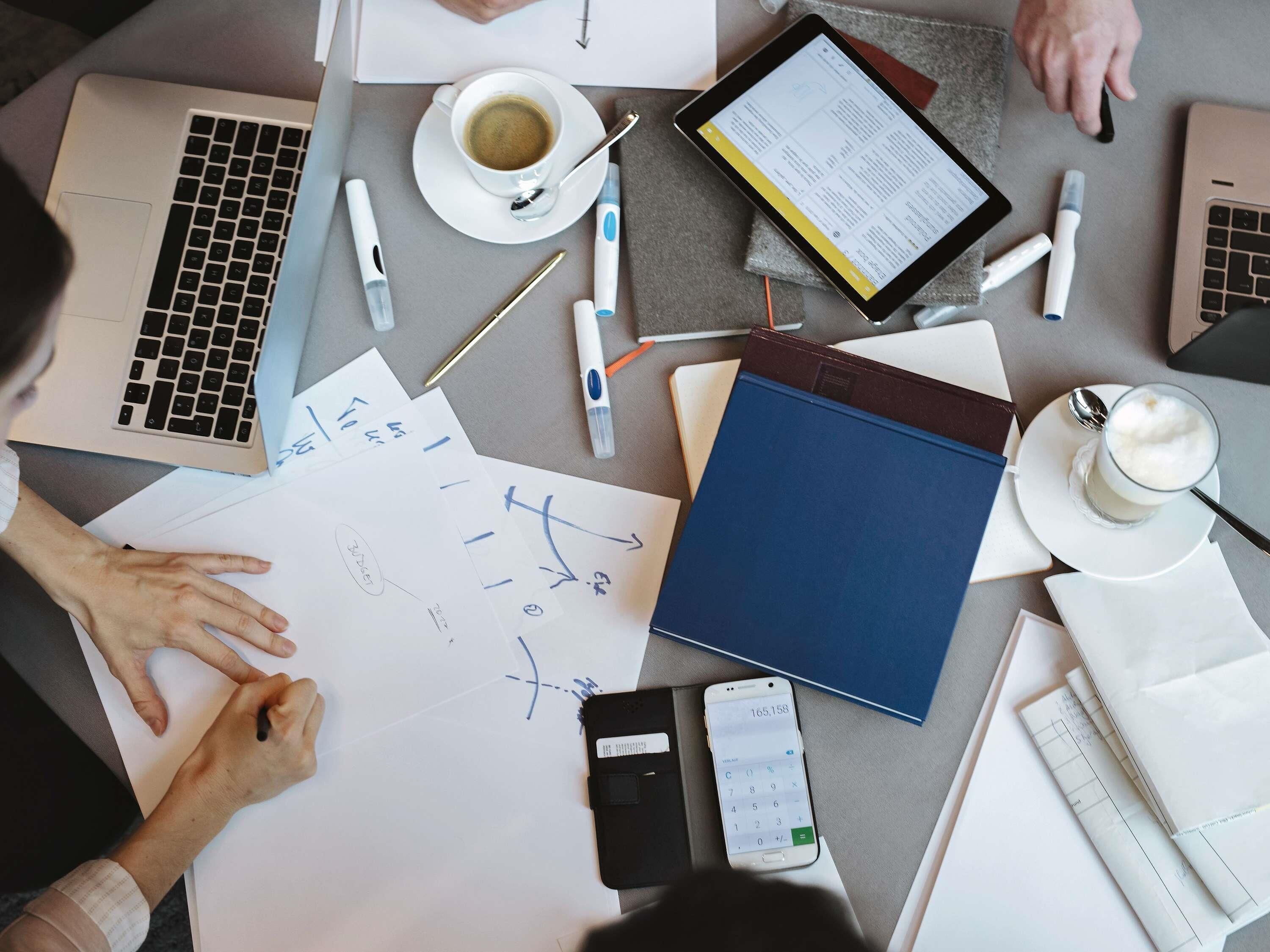 A workspace with a laptop, documents, a smartphone, a tablet, a cup of coffee, and writing instruments.