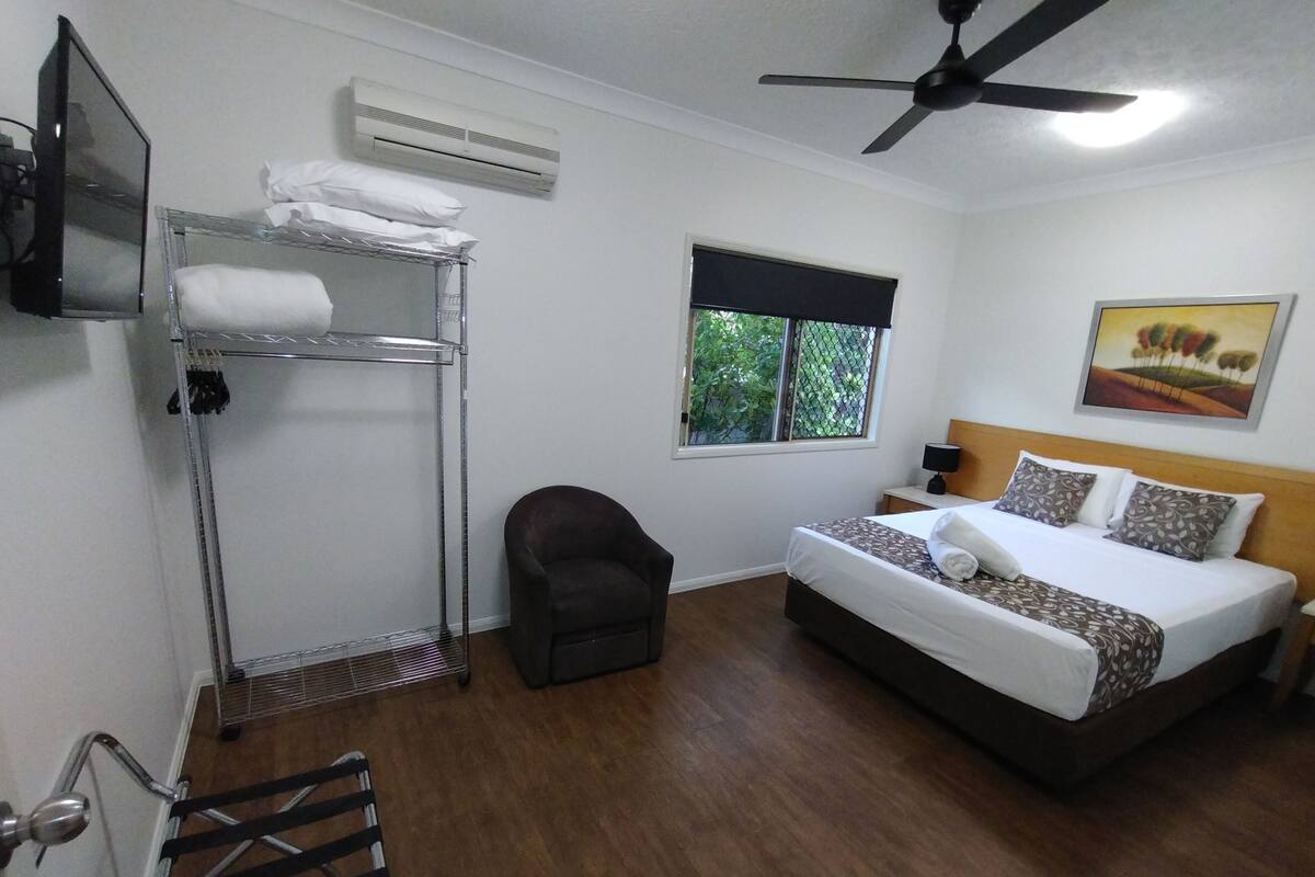 A bedroom with a bunk bed, a single bed, a chair, a window with a view, an air conditioner, and a ceiling fan.