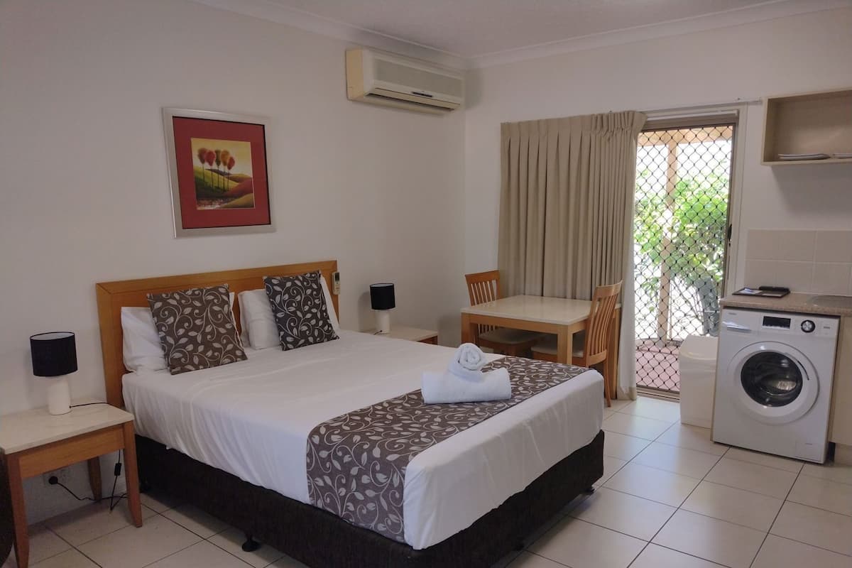 A hotel room with a bed, a table with chairs, a washing machine, and an air conditioning unit.