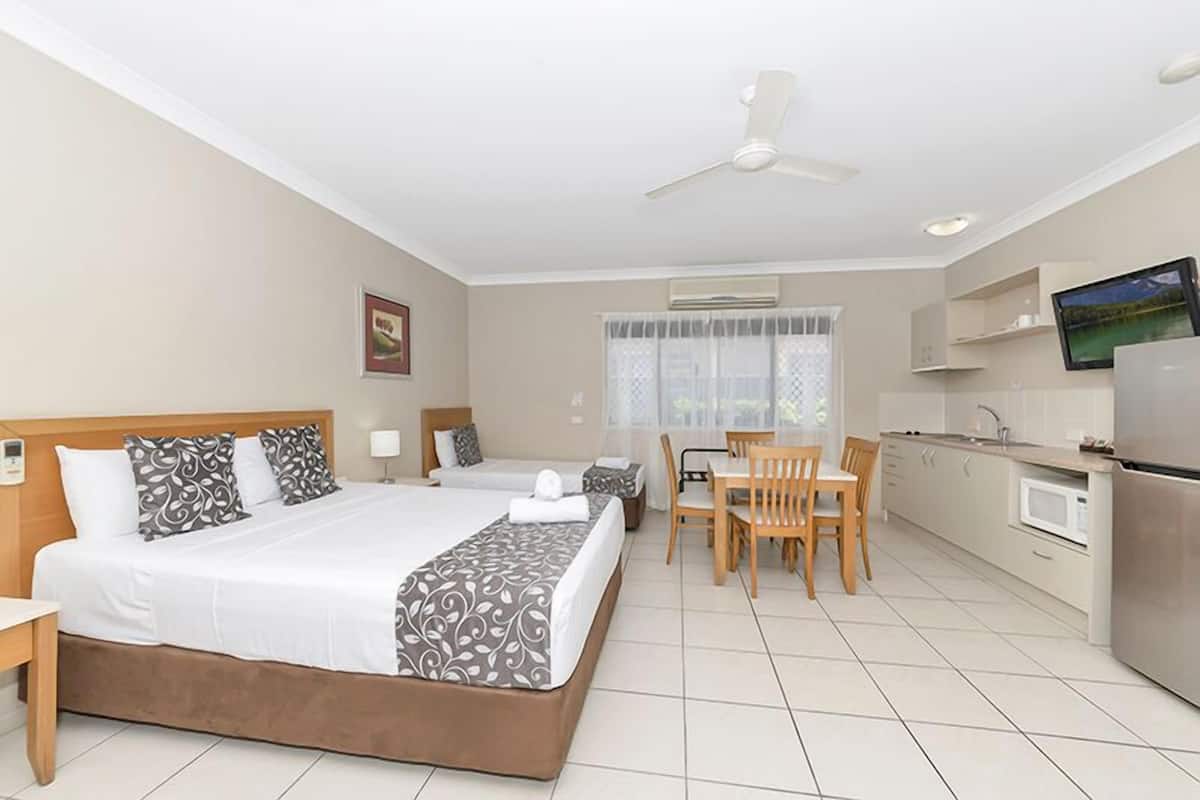 A hotel room with a bed, a desk, a chair, a television, and a kitchenette.