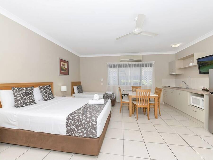 A hotel room with a bed, a desk, a chair, a television, and a kitchenette.