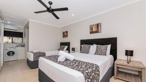 Una habitación de hotel con una cama grande, una cama más pequeña, una lavadora y un ventilador de techo.