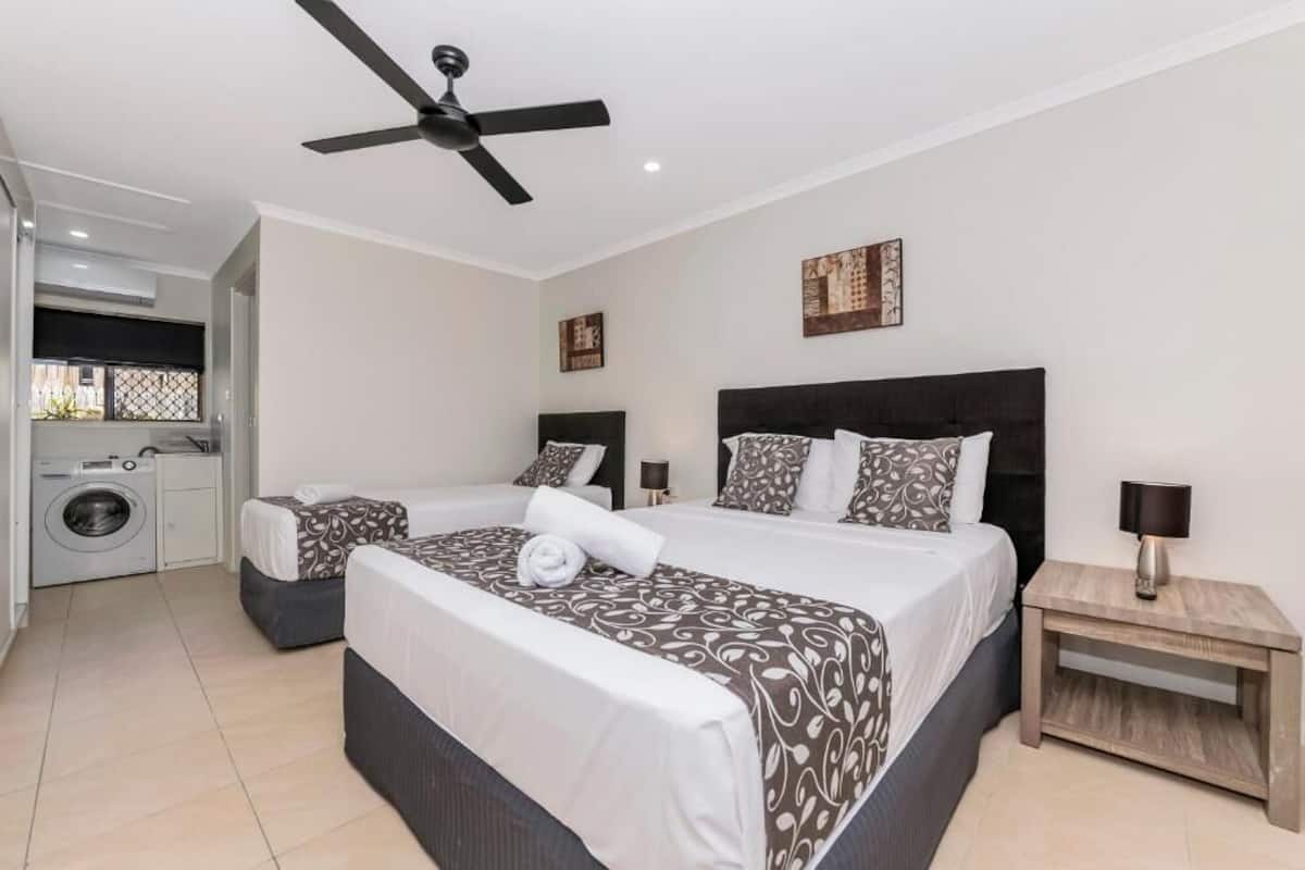 A hotel room with a large bed, a smaller bed, a washing machine, and a ceiling fan.