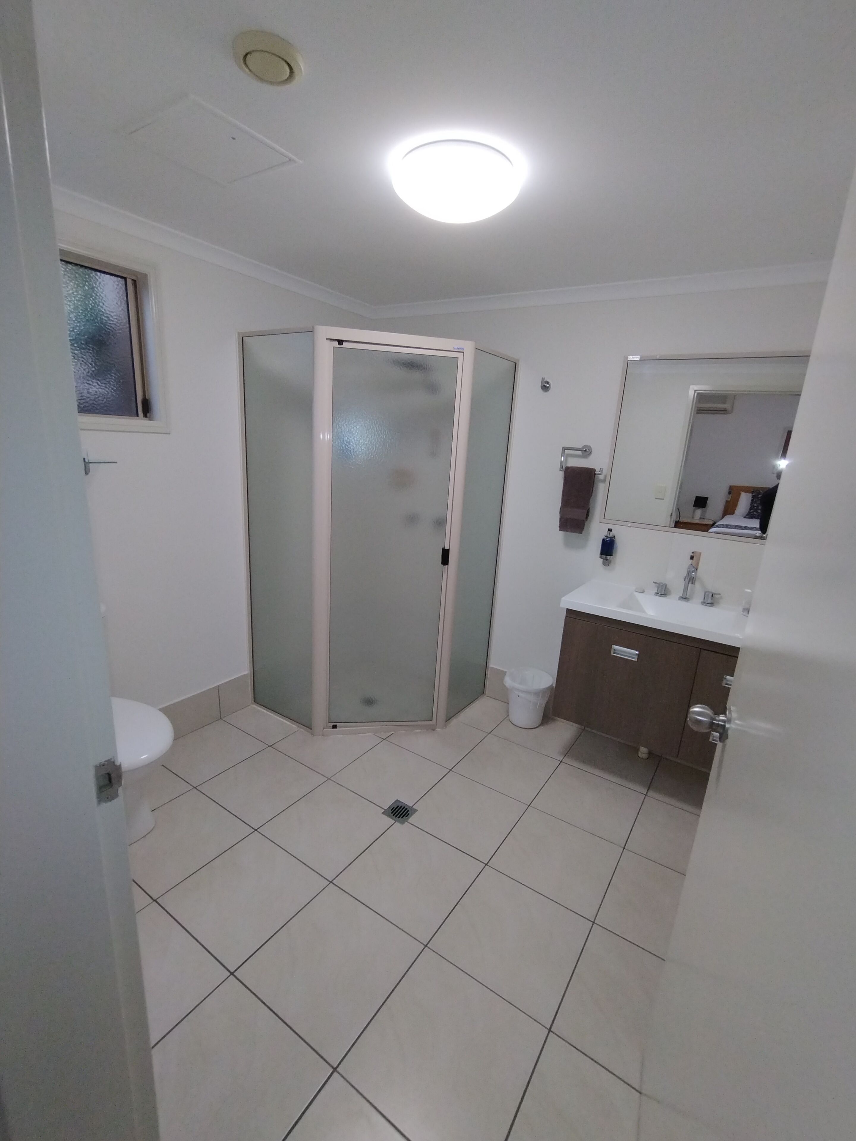 A bathroom with a toilet, a sink, a mirror, and a shower enclosure.