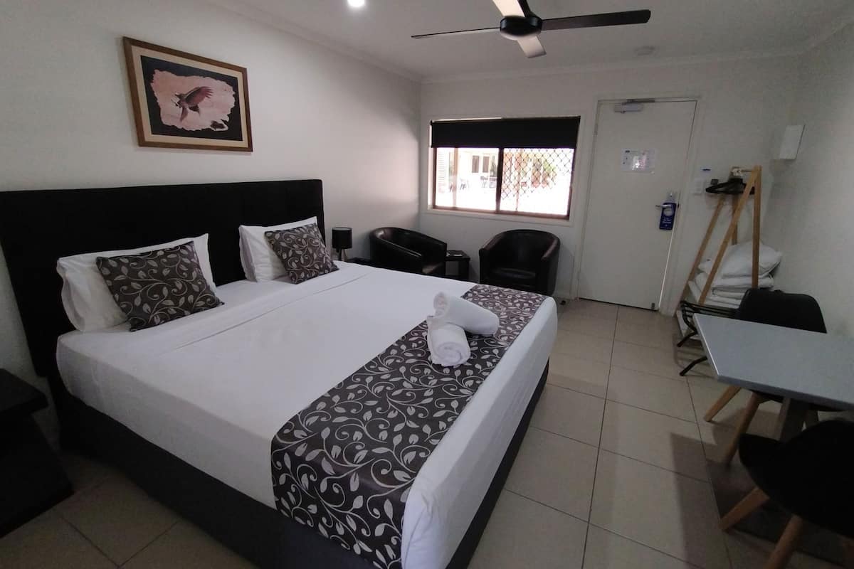 A hotel room with a bed, a desk, a chair, a ceiling fan, and a window with a view.
