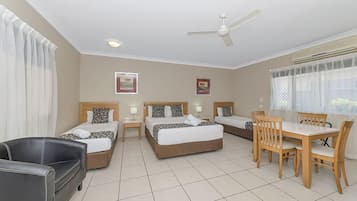 Een hotelkamer met twee bedden, een eettafel met stoelen, een zwarte leren bank en een plafondventilator.