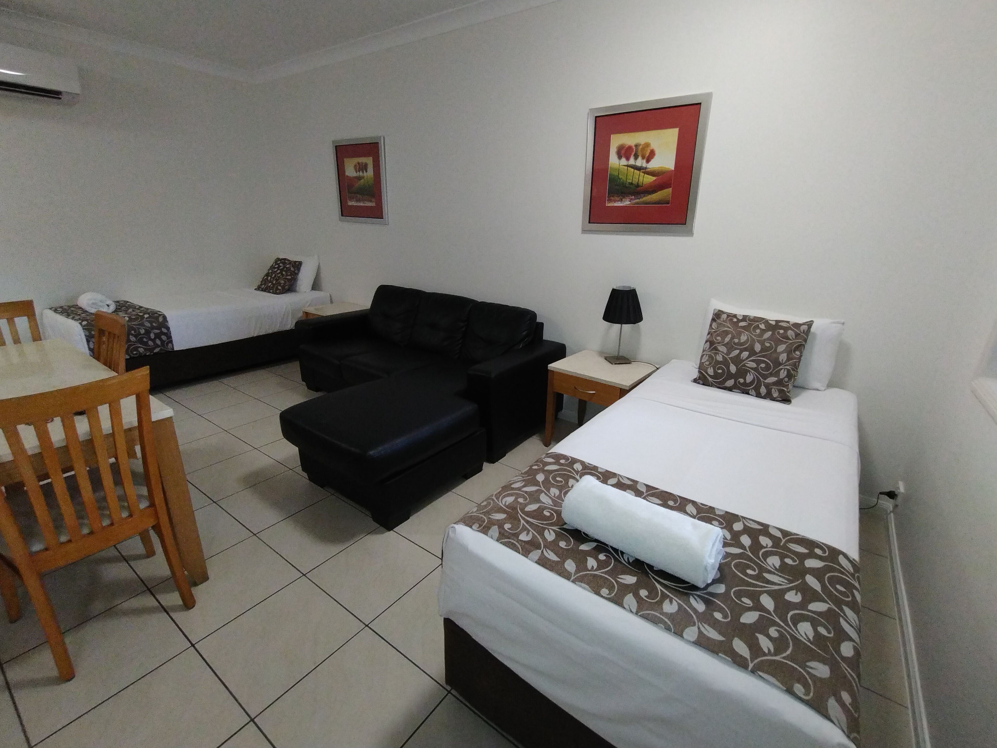 A hotel room with two beds, a sofa, a dining table, and a small table with a lamp.