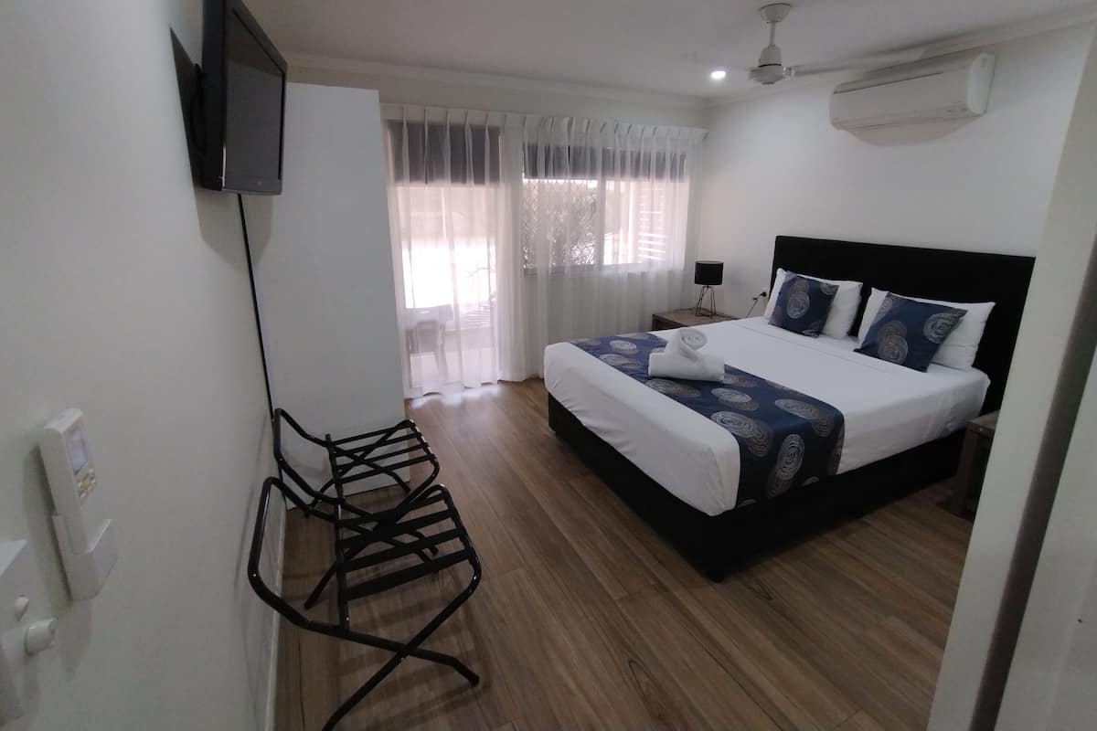 A hotel room with a bed, a TV mounted on the wall, a ceiling fan, and a window with curtains.