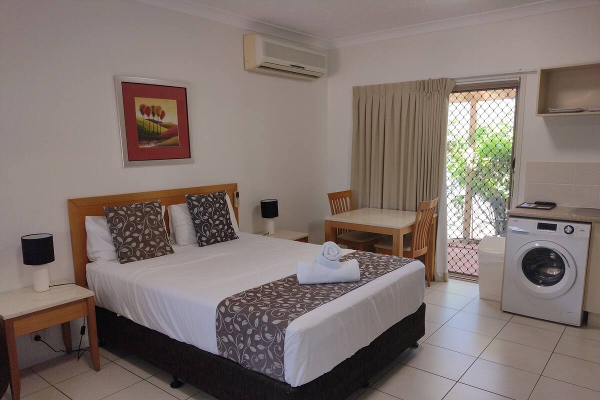 A hotel room with a bed, bedside tables, a table with chairs, a washing machine, and a picture on the wall.
