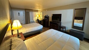 Ein Hotelzimmer mit zwei Betten, einem Schreibtisch, einem Fernseher, einem Spiegel und einer Lampe.