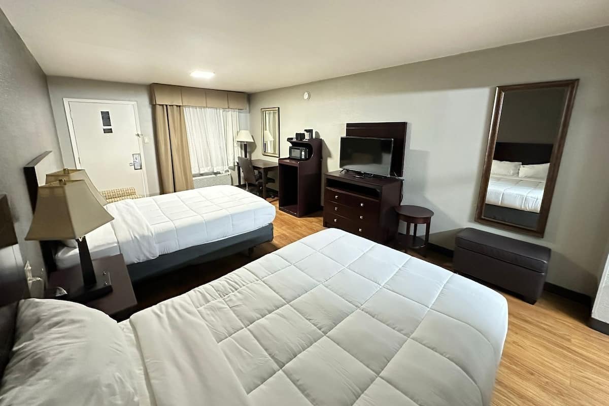 A hotel room with two beds, a desk, a TV, a mirror, and a wardrobe.