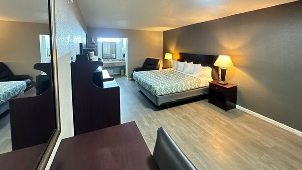 A hotel room with a bed, bedside tables, a desk, a chair, and a large mirror.