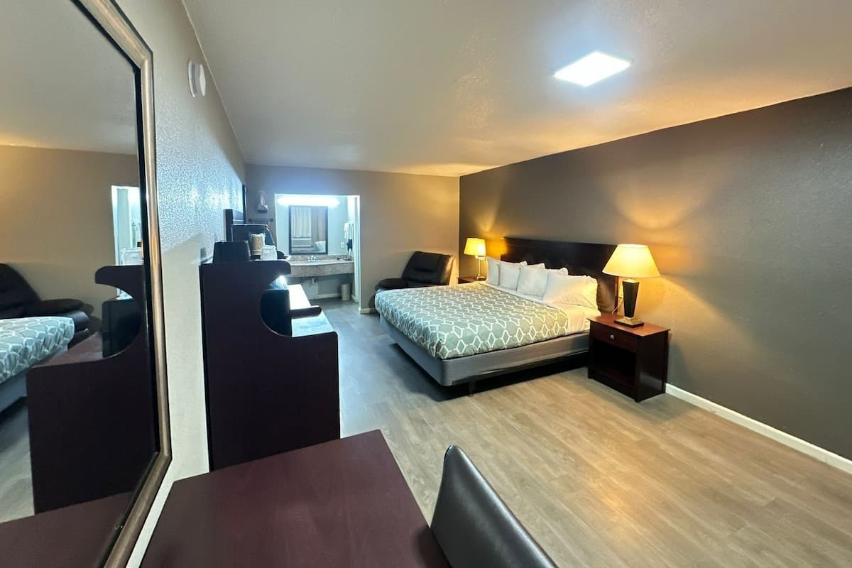 A hotel room with a bed, bedside tables, a desk, a chair, and a large mirror.