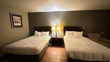 Une chambre d’hôtel avec deux lits, une table de chevet avec une lampe, un tableau encadré au mur et une chaise à motifs.